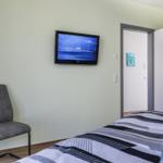 Ein Schlafzimmer mit Bett, Stuhl und Wandfernseher. An der Wand hängt ein Bild.