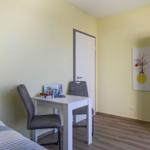 Ein Zimmer mit Bett, Schreibtisch, Stühlen und Kleiderschrank an der Wand.