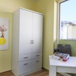 Ein Raum mit weißen Schränken, einem Tisch und einem Fenster mit grünen Jalousien.