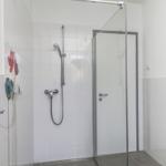 Dusche mit Glaswand, Duschbrause und Heizkörper mit Handtuch.