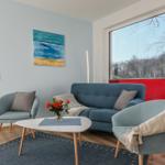 Ein Wohnzimmer mit blauem Sofa, zwei Sesseln und einem weißen Tisch. An den Wänden hängt ein Bild.