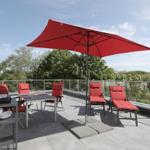 Terrasse mit rotem Sonnenschirm und Sitzgelegenheiten, Blick auf grüne Bäume.