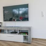 TV auf Wandhalterung, Unterputz mit Spielboxen und Buchern.