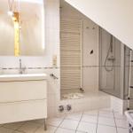 Badezimmer mit Dusche, Waschbecken und Heizkörper unter Dachschrägen.