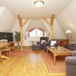 Wohn- und Essbereich mit Holzdielen, Sitzgruppe und Fernseher unter schrägen Dachbalken.