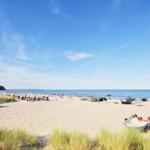 Strand mit Sand, Booten und Strandkörben unter blauem Himmel.