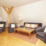 Wohnzimmer mit grauen Sesseln, Sofa und Holztisch. Holzdecke und Fenster mit Vorhängen.