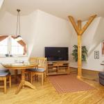 Wohnzimmer mit Essbereich, Fernseher und Holzfußboden. Zwei Fenster mit Vorhängen.