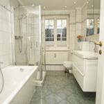 Badezimmer mit Badewanne, Dusche, Waschbecken und Toilette. Fenster mit Blick nach draußen.