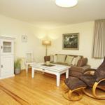 Wohnzimmer mit braunem Sofa, Schwebestuhl und weißen Möbeln auf Holzboden.