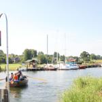 Boot fährt auf Fluss mit Yachten und Uferhäusern