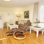 Wohnzimmer mit braunem Sofa, weißem Tisch und Holzboden. Fenster mit weißen Vorhängen.