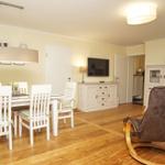 Essbereich mit weißem Tisch und Stühlen, Fernseher und Schaukelsessel im Wohnbereich.