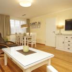 Wohn- und Essbereich mit Holzboden, TV, Esstisch und Sessel.