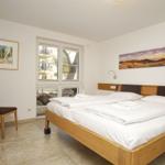 Schlafzimmer mit Bett, Stuhl und Fenster. Wandbilder und Beleuchtung.