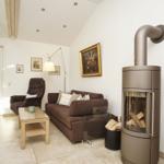 Wohnzimmer mit Sofa, Sessel, Kamin und Glasfront zur Außenterrasse.