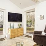 Wohnzimmer mit Fernseher, braunem Sessel und Glasfronten zur Außenterrasse.