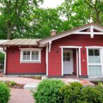 Rotes Haus mit weißen Fensterrahmen und Terrasse unter Bäumen.
