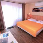 Schlafzimmer mit Doppelbett, Schreibtisch und großen Fenstern mit Vorhängen.