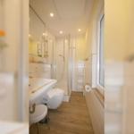 Badezimmer mit Dusche, WC und Waschbecken. Holzfußboden und Fenster.