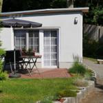 Wohnung mit Terrasse, Sonnenschutz, Tisch und Stühle. Grünanlage und gepflasterte Fläche.