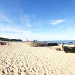 Strand mit Booten und Liegestühlen unter blauem Himmel.