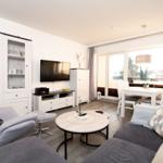 Wohn- und Essbereich mit Sofa, Sessel, Esstisch und TV. Balkon mit Sicht auf Grün.