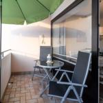 Terrasse mit grünem Sonnenschirm, Tisch und zwei Stühlen. Durchgang in Wohnbereich mit Sofa und Tisch.