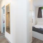 Schlafzimmer mit Bett, Fenster und Spiegel. Flur mit Wandbild und Aufbewahrungsbox.