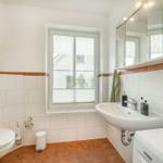 Badezimmer mit Toilette, Waschbecken und Fenster. Wand- und Bodenfliesen in Weiß und Terrakotta.