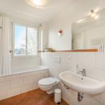 Badezimmer mit Badewanne, Dusche, Waschbecken und Toilette. Fenster mit Blick nach draußen.