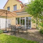 Terrasse mit Tisch, Stühlen und Sonnenschirm vor gelbem Haus mit Glasfront.