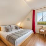 Schlafzimmer mit Dachschrägen, Bett, Nachttisch, Stuhl und Fenster.