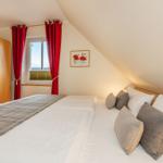 Schlafzimmer mit Dachschrägen, Bett mit Kissen, rote Vorhänge und Fenster.