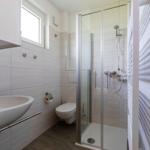 Badezimmer mit Dusche, Toilette und Waschbecken. Fliesenwand und Fenster sichtbar.