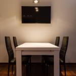 Esszimmer mit weißem Tisch, vier schwarzen Stühlen und Wand-TV unter einer Deckenleuchte.