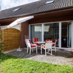 Terrasse mit Tisch, Stühlen und Sonnenschirm. Hintergrund: Haus mit Glasfront und Holzzaun.