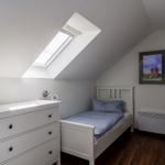 Schlafzimmer mit Dachschrägen, Dachfenster, weißem Bett und Kleiderschrank.