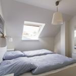 Schlafzimmer mit Dachfenster, Bett, Spiegel und Deckenleuchte.