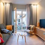 Wohnzimmer mit Sofa, Sessel und Fernseher. Durchgang zur Terrasse mit Blick auf Wohnhäuser.