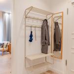 Eingangsbereich mit Garderobe, Spiegel und Sitzbank. Im Hintergrund ist ein Wohnbereich mit Sessel und Tisch.