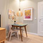 Essbereich mit Tisch, Stühlen und Wandbildern. Fernseher auf Holzregal.