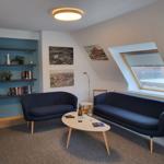 Zwei blaue Sofas stehen in einem Raum mit Dachfenster und Bücherregal an der Wand.