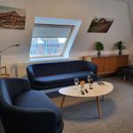 Wohnzimmer mit blauer Couch, Tisch und Dachfenster. Wandbilder und Pflanzen.