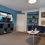 Wohnzimmer mit Fernseher, Sofa und Tisch. Wand mit Regalen und Bildern.