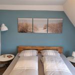 Schlafzimmer mit Doppelbett, blauer Wand und drei Strandbildern.