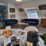 Wohnbereich mit zwei dunkelblauen Sofas, Tisch und Blick auf Dachfenster.