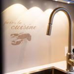 Küchenzeile mit Wasserhahn und Wanddekoration mit Krabbe und Schriftzug.