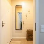 Eingangsbereich mit Spiegel, Haken und Korb. Holzdielen und weiße Wände.