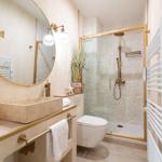 Badezimmer mit Dusche, Waschtisch und Toilette. Holzrahmen und goldfarbene Armaturen.